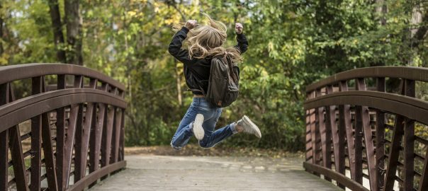 Girl with backpack jumping on a bridge